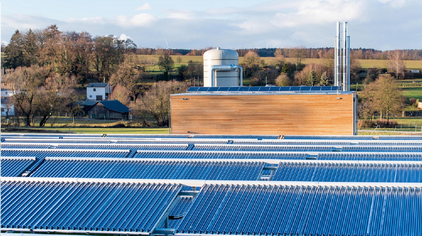 Zu sehen ist im Vordergrund das Kollektorfeld der Solarthermie-Anlage und im Hintergrund die Heizzentrale des Dorf-Fernwärme-Netzes in Ellern/Hunsrück.